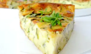 Tranche de clafoutis courgettes dorée et moelleuse, garnie de quelques feuilles de basilic frais.