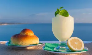 Colazione siciliana con brioche e granita al limone, con il mare e l'Etna sullo sfondo.