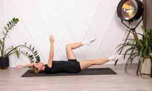 Donna esegue esercizi per mal di schiena lombare su un tappetino. Gambe sollevate, braccia tese.