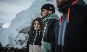 Trzy osoby w zimowej scenerii. Kobieta w dwukolorowej bluzie, obok mężczyźni w bluzach narciarskich męskich.