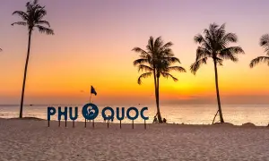 Zachód słońca na plaży Phu Quoc, Wietnam. Palmy i napis "PHU QUOC" na tle pomarańczowego nieba.