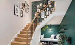 Un habillage mural de cage d'escalier avec une galerie de cadres et un papier peint géométrique vert. Un banc confortable est aménagé sous l'escalier.