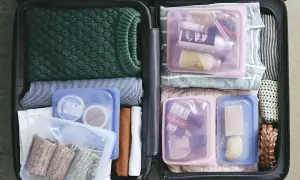 Pakowanie do samolotu: zielony sweter, paski, kosmetyki w woreczkach, skarpetki i balsamy.