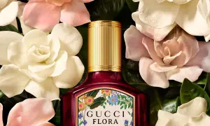 Perfumy Gucci by Gucci Flora w otoczeniu delikatnych kwiatów. Złota nakrętka i bogata etykieta z motywem roślinnym.