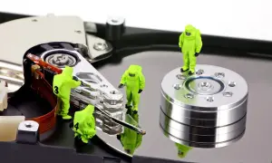 Miniaturowe figurki w kombinezonach pracują nad dyskiem twardym, symbolizując odzyskiwanie danych z dysku.