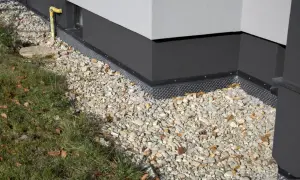 Folia kubełkowa chroni fundament do wysokości ok. 30 cm. Widać ją pod warstwą żwiru i trawą.
