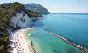 Spiaggia di Marina Palmense con scogliere bianche, mare azzurro e ombrelloni colorati.