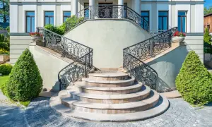 Imponente villa con scale esterne coperte da ringhiere in ferro battuto e ornate da vasi con fiori rossi.