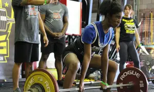 Atleta si prepara per uno stacco da terra, concentrata. Un evento di powerlifting e weightlifting con pubblico e attrezzature.