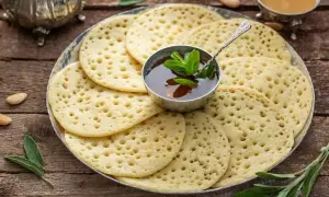 Une assiette de crêpes mille trous dorées, garnie d'une coupelle de miel et de menthe fraîche. Parfait pour un petit-déjeuner gourmand.