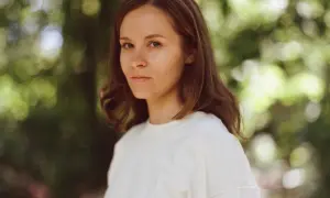 Hania Rani Esja, artystka o hipnotyzującym spojrzeniu, w białej bluzie na tle zieleni.