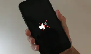 Dłoń trzyma czarny iPhone z ikoną wyciszenia. Rozmówca jest słabo słyszalny.