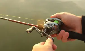 Dłonie trzymają wędkę z kołowrotkiem, gotowe do rzutu. Precyzyjne **casting spinning** to klucz do sukcesu.