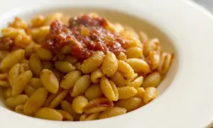 Malloreddus alla campidanese, pasta sarda con sugo di pomodoro e salsiccia, serviti in un piatto bianco.