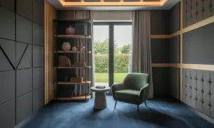 Pannelli fonoassorbenti su pareti e soffitto, poltrona verde, libreria e tappeto blu creano un ambiente ideale per capire come insonorizzare una stanza.