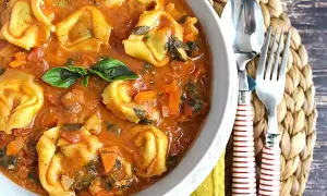 Miseczka tortellini w sosie pomidorowym z bazylią, obok sztućców.