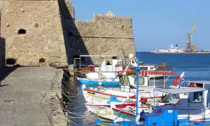 Port w Rethymno na Krecie w listopadzie. Kamienna twierdza i kolorowe łodzie cumujące w spokojnej zatoce.
