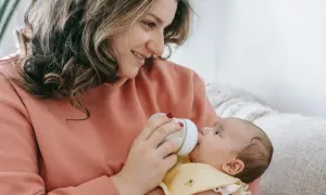 Uśmiechnięta mama karmi butelką dziecko. Warto wiedzieć, ile odciągnięte mleko może stać w lodówce, by zapewnić mu bezpieczeństwo.