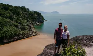 Ein Paar genießt die Aussicht auf eine tropische Bucht mit Sandstrand und Dschungel. Tolle Malaysia Urlaub Erfahrungen!