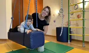 Kobieta i chłopiec w sali terapeutycznej z huśtawką i drabinką.