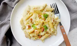 Penne z kremowym sosem z kalafiora, orzechami i natką pietruszki. Pyszny makaron z kalafiorem na białym talerzu.