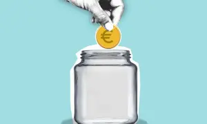 Eine Hand wirft eine Münze mit Euro-Symbol in ein leeres Glas. Sparen für den hauskauf steuer absetzen.