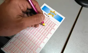 Ręka z ołówkiem zaznacza liczby na kuponie Lotto. Dowiedz się, lotto plus na czym polega dodatkowe losowanie i jak zwiększyć szanse na wygraną.