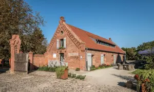 Dawny folwark w Wąsowie, dziś restauracja. Ceglany budynek z czerwonym dachem, kamienna nawierzchnia i zielone otoczenie.