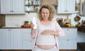 Kobieta w ciąży trzyma butelkę mleka, czując ból serca. Jej twarz wyraża dyskomfort, a dłoń spoczywa na brzuchu.