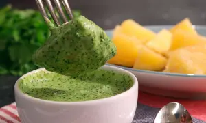 Un tenedor recoge una porción de mojo verde canario, una salsa vibrante, junto a papas arrugadas.