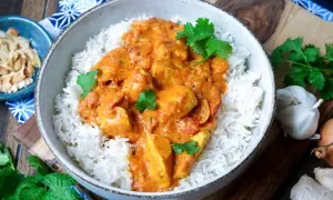 Schüssel mit duftendem Reis und cremigem Chicken Tikka, garniert mit frischem Koriander. Daneben Mandelsplitter, Knoblauch und Ingwer.