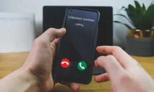 Dłoń trzyma smartfon, na ekranie którego widnieje komunikat "Unknown number calling...". Numer prywatny dzwoni, a użytkownik zastanawia się, czy odebrać.