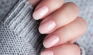 Delikatne, różowe paznokcie na tle szarego swetra. Dowiedz się, jak stosować bazę kauczukową Niuqi dla idealnego manicure.