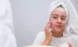 Dziewczyna z ręcznikiem na głowie nakłada krem na twarz. Witamina A pod oczy może pomóc w pielęgnacji skóry.