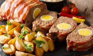 Pyszny klops z jajkiem w środku, zawinięty w boczek, podany z pieczonymi ziemniakami i warzywami.