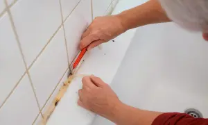 Ręce usuwają stary, zabrudzony silikon z wanny za pomocą nożyka. Dowiedz się, jak usunąć silikon z materiału, aby odnowić łazienkę.