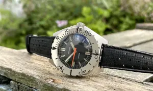 Reloj Sandoz Geneve Typhoon con correa negra, sobre madera rústica y fondo verde.