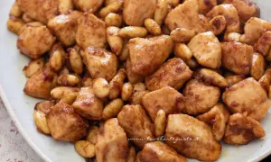 Un invitante pollo alle mandorle, con bocconcini dorati e mandorle tostate, servito su un piatto bianco.