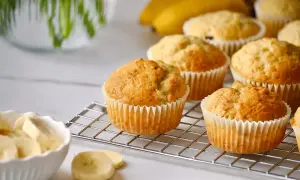 Frisch gebackene bananen muffins auf einem Kuchengitter, daneben eine Schüssel mit Bananenstücken.
