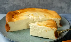 Ein saftiger Quarkkuchen ohne Boden, goldbraun gebacken, liegt auf einem Teller. Ein Stück ist bereits angeschnitten und zeigt die cremige Konsistenz.