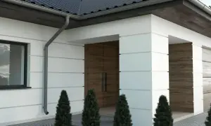 Nowoczesny dom z białymi boniami, drewnianymi drzwiami i ciemnym dachem.