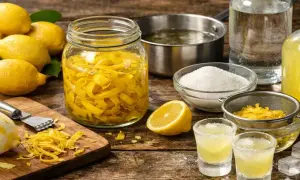 Préparation de la recette limoncello : citrons, écorces macérant dans un bocal, sucre, alcool et verres prêts à déguster.
