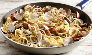Un piatto invitante di spaghetti con le vongole, condito con prezzemolo fresco, servito in una padella su un tavolo di legno.