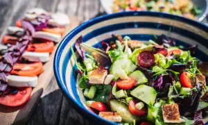 En matig sallad med allt om mat: färska grönsaker, krutonger och mozzarella på en träplanka.