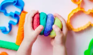 Kinderhände halten bunte Knetmasse, bereit zum Kneten. Nebenan liegen bunte Ausstecher, perfekt zum Knetseife selber machen.