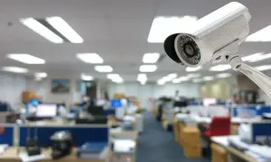 Kamera monitoringu w biurze, kontrola pracownika. Widok na rzędy biurek i oświetlenie sufitowe.