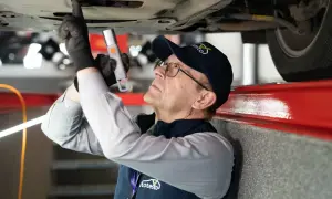 Mechanik w czapce z logo "autotesto.pl" sprawdza podwozie auta, szukając usterek. To kluczowe dla rankingu najlepszych firm od sprawdzania auta przed zakupem.