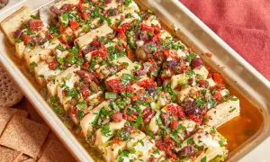 Un plat de fromage blanc coupé en tranches, garni d'olives, de tomates séchées et d'herbes. Une excellente idée repas pour l'apéritif.