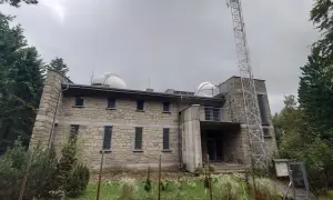 Obserwatorium na Lubomirze, kamienny budynek z kopułami teleskopów i wieżą telekomunikacyjną, otoczony zielenią.