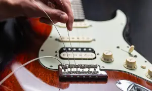 Dłoń naciąga nowe struny w gitarze elektrycznej, przygotowując ją do gry.